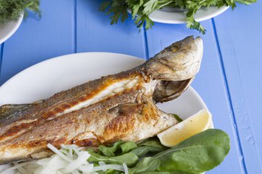 Yeşil ve mavi ahşap masa, deniz ürünleri kavramı üzerinde limon ile ızgara levrek balık