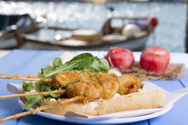 Lezzetli altın derin kızarmış pirzola midye şişleri yoğurt sos tartar ile hizmet veren sandviç, domates, dilimlenmiş beyaz soğan, maydanoz ve yeşil roka salatası mavi rustik masa arka plan üzerinde. Midye tava ekmek.