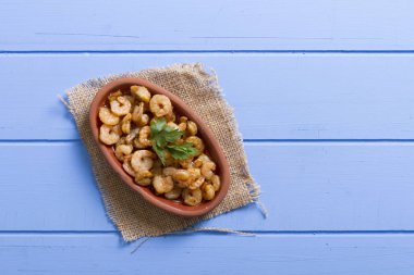 Lezzetli küçük kırmızı karides tereyağı ile baharat baharat haşlanmış. Geleneksel Yunan çanak çömlek içinde hizmet veren karides güveç. Üstten görünüm mavi rustik arka plan. En ortak gıda alerjenleri arasında diğer kabuklu deniz ürünleri.