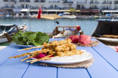 Lezzetli altın derin kızarmış pirzola midye yoğurt sos tartar ile hizmet veren şişleri, domates, dilimlenmiş beyaz soğan, maydanoz ve yeşil roka salatası mavi rustik masa arka plan üzerinde. Midye tava.