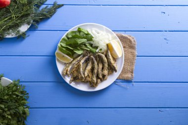 Tabak kızarmış taze mevsimlik otlar, hafif mavi ahşap masa dilimlenmiş soğan, roka, maydanoz ve limon ile hizmet veren kırmızı kefal balık. Mullus subtropikal deniz aile Levreksiler balık cinsidir.
