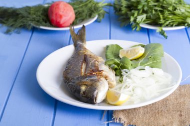 Yeşil ve mavi ahşap masa, deniz ürünleri kavramı üzerinde limon ile ızgara dorado balık