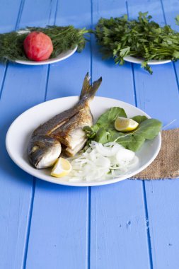 Yeşil ve mavi ahşap masa, deniz ürünleri kavramı üzerinde limon ile ızgara dorado balık