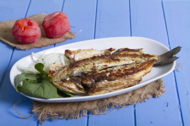 Lezzetli ızgara fileto levrek porsiyon dilimlenmiş soğan, domates, yeşil roka salatası ve sulu limon rustik mavi ahşap masa arka plan üzerinde oval beyaz plakalı füme. Alan, kopyalama kimse.