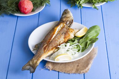 Yeşil ve mavi ahşap masa, deniz ürünleri kavramı üzerinde limon ile ızgara levrek balık