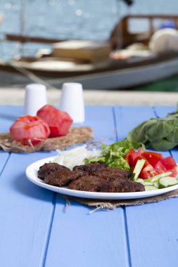 Izgara sığır eti köfte porsiyon dilimlenmiş salatalık, beyaz soğan, küp daire plakalı domates ve marul salatası mavi rustik ahşap masanın üstüne kesmek. Ekmek kırıntıları, tereyağı ve baharat gibi maddeler.