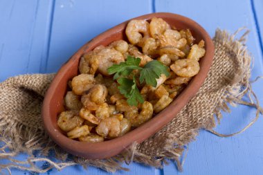 Lezzetli küçük kırmızı karides tereyağı ile baharat baharat haşlanmış. Geleneksel Yunan çanak çömlek içinde hizmet veren karides güveç. Üstten görünüm mavi rustik arka plan. En ortak gıda alerjenleri arasında diğer kabuklu deniz ürünleri.