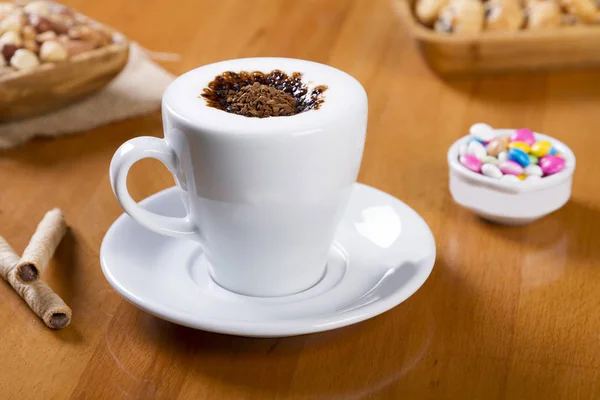 Cup of Black Instant Coffee with milk foam in white cup serving on wood table with chocolate, bonbons  and nuts. Instant Coffee also called soluble coffee