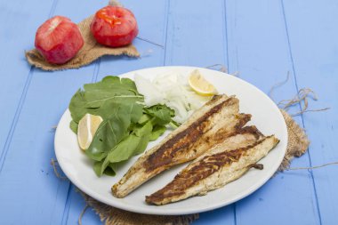 Lezzetli ızgara fileto levrek porsiyon dilimlenmiş soğan, domates, yeşil roka salatası ve sulu limon rustik mavi ahşap masa arka plan üzerinde oval beyaz plakalı füme. Alan, kopyalama kimse.