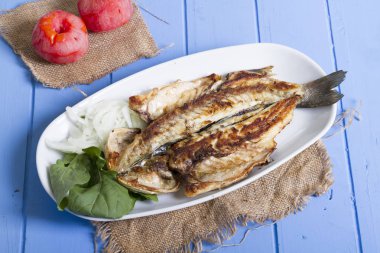 Lezzetli ızgara fileto levrek porsiyon dilimlenmiş soğan, domates, yeşil roka salatası ve sulu limon rustik mavi ahşap masa arka plan üzerinde oval beyaz plakalı füme. Alan, kopyalama kimse.