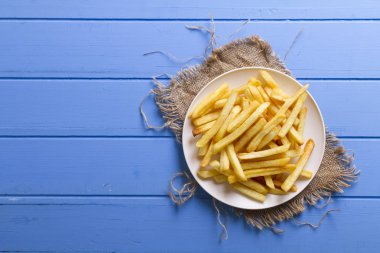 Lezzetli altın Ev yapımı Deep Fried tuzlu beyaz hizmet patates kızartması plaka rustik mavi ahşap masa arka plan üzerinde yuvarlak. Parmağı cipsi veya patates batonnet veya allumette derin kızarmış patates kesmek. 