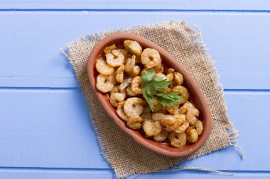 Lezzetli küçük kırmızı karides tereyağı ile baharat baharat haşlanmış. Geleneksel Yunan çanak çömlek içinde hizmet veren karides güveç. Üstten görünüm mavi rustik arka plan. En ortak gıda alerjenleri arasında diğer kabuklu deniz ürünleri.