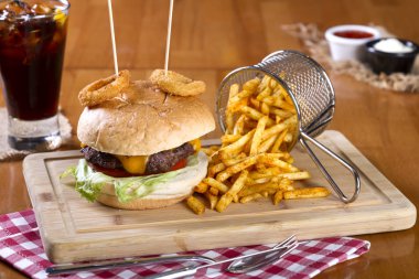 Ev yapımı hamburger marul, soğan, mantar, domates dilimleri, turşu, pastırma ve kaşar peynir porsiyon kızarmış baharatlı patates kızartması ile ahşap masa arka plan üzerinde.