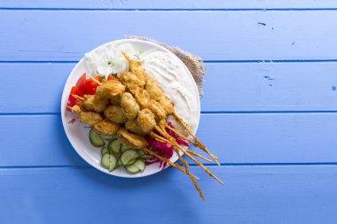 Lezzetli altın derin kızarmış pirzola midye yoğurt sos tartar ile hizmet veren şişleri, domates, dilimlenmiş beyaz soğan, maydanoz ve yeşil roka salatası mavi rustik masa arka plan üzerinde. Midye tava.