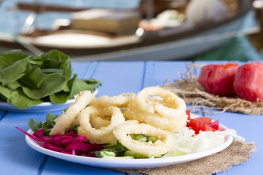 Lezzetli derin kızarmış kalamar garson beyaz daire plaka, kırmızı lahana, tartar, halka dilimlenmiş soğan ve yeşil roka salatası rustik mavi ahşap arka plan üzerinde. Kalamar çok mutfaklarının yemek. Üstten görünüm.