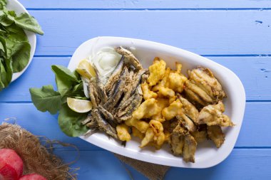 Lezzetli derin kızarmış Mix deniz ürünleri balık plaka mezgit, hamsi, sardalya, mavi rustik ahşap arka plan üzerinde beyaz soğan, limon, domates, roka salatası dilimlenmiş.