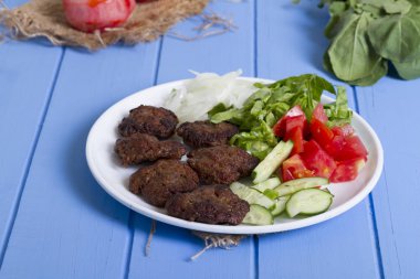 Izgara sığır eti köfte porsiyon dilimlenmiş salatalık, beyaz soğan, küp daire plakalı domates ve marul salatası mavi rustik ahşap masanın üstüne kesmek. Ekmek kırıntıları, tereyağı ve baharat gibi maddeler.