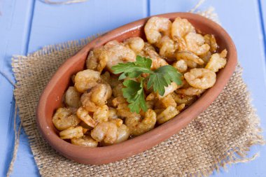 Lezzetli küçük kırmızı karides tereyağı ile baharat baharat haşlanmış. Geleneksel Yunan çanak çömlek içinde hizmet veren karides güveç. Üstten görünüm mavi rustik arka plan. En ortak gıda alerjenleri arasında diğer kabuklu deniz ürünleri.