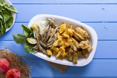 Lezzetli derin kızarmış Mix deniz ürünleri balık plaka mezgit, hamsi, sardalya, mavi rustik ahşap arka plan üzerinde beyaz soğan, limon, domates, roka salatası dilimlenmiş.