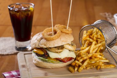 Ev yapımı hamburger marul, soğan, mantar, domates dilimleri, turşu, pastırma ve kaşar peynir porsiyon kızarmış baharatlı patates kızartması ile ahşap masa arka plan üzerinde.