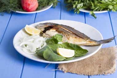 Yeşil ve mavi ahşap masa, deniz ürünleri kavramı üzerinde limon ile ızgara dorado balık