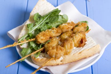 Lezzetli altın derin kızarmış pirzola midye şişleri yoğurt sos tartar ile hizmet veren sandviç, domates, dilimlenmiş beyaz soğan, maydanoz ve yeşil roka salatası mavi rustik masa arka plan üzerinde. Midye tava ekmek.