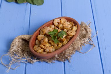 Lezzetli küçük kırmızı karides tereyağı ile baharat baharat haşlanmış. Geleneksel Yunan çanak çömlek içinde hizmet veren karides güveç. Üstten görünüm mavi rustik arka plan. En ortak gıda alerjenleri arasında diğer kabuklu deniz ürünleri.