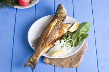 Yeşil ve mavi ahşap masa, deniz ürünleri kavramı üzerinde limon ile ızgara levrek balık