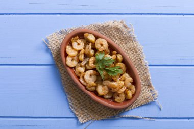 Lezzetli küçük kırmızı karides tereyağı ile baharat baharat haşlanmış. Geleneksel Yunan çanak çömlek içinde hizmet veren karides güveç. Üstten görünüm mavi rustik arka plan. En ortak gıda alerjenleri arasında diğer kabuklu deniz ürünleri.