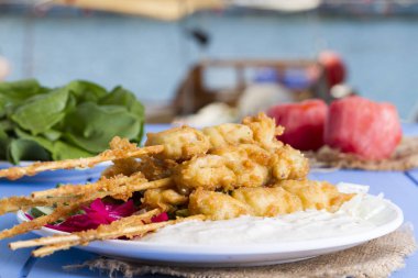 Lezzetli altın derin kızarmış pirzola midye yoğurt sos tartar ile hizmet veren şişleri, domates, dilimlenmiş beyaz soğan, maydanoz ve yeşil roka salatası mavi rustik masa arka plan üzerinde. Midye tava.