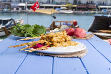 Lezzetli altın derin kızarmış pirzola midye yoğurt sos tartar ile hizmet veren şişleri, domates, dilimlenmiş beyaz soğan, maydanoz ve yeşil roka salatası mavi rustik masa arka plan üzerinde. Midye tava.