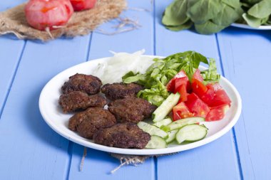 Izgara sığır eti köfte porsiyon dilimlenmiş salatalık, beyaz soğan, küp daire plakalı domates ve marul salatası mavi rustik ahşap masanın üstüne kesmek. Ekmek kırıntıları, tereyağı ve baharat gibi maddeler.
