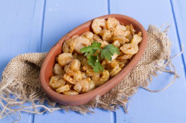 Lezzetli küçük kırmızı karides tereyağı ile baharat baharat haşlanmış. Geleneksel Yunan çanak çömlek içinde hizmet veren karides güveç. Üstten görünüm mavi rustik arka plan. En ortak gıda alerjenleri arasında diğer kabuklu deniz ürünleri.