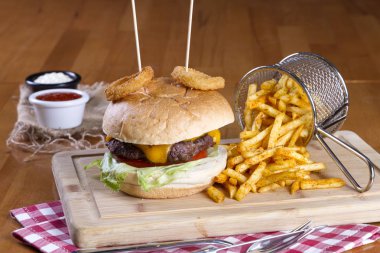 Ev yapımı hamburger marul, soğan, mantar, domates dilimleri, turşu, pastırma ve kaşar peynir porsiyon kızarmış baharatlı patates kızartması ile ahşap masa arka plan üzerinde.