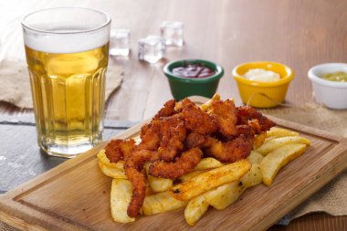 Soğuk köpüklü altın soğutulmuş taslak bira hizmet plakalı lezzetli sıcak gevrek ev yapımı taze kızarmış tavuk kanatları, dilimlenmiş domuz sosisi ve kişiler üzerine ahşap bambu tahta baharatlı sos ile.