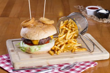 Ev yapımı hamburger marul, soğan, mantar, domates dilimleri, turşu, pastırma ve kaşar peynir porsiyon kızarmış baharatlı patates kızartması ile ahşap masa arka plan üzerinde.