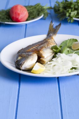 Yeşil ve mavi ahşap masa, deniz ürünleri kavramı üzerinde limon ile ızgara dorado balık