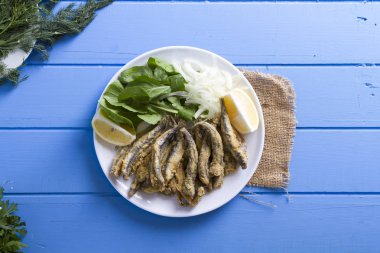 Tabak kızarmış taze mevsimlik otlar, hafif mavi ahşap masa dilimlenmiş soğan, roka, maydanoz ve limon ile hizmet veren kırmızı kefal balık. Mullus subtropikal deniz aile Levreksiler balık cinsidir.