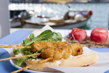 Lezzetli altın derin kızarmış pirzola midye şişleri yoğurt sos tartar ile hizmet veren sandviç, domates, dilimlenmiş beyaz soğan, maydanoz ve yeşil roka salatası mavi rustik masa arka plan üzerinde. Midye tava ekmek.