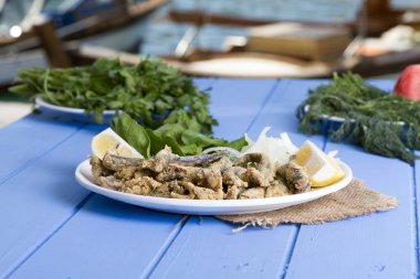 Tabak kızarmış taze mevsimlik otlar, hafif mavi ahşap masa dilimlenmiş soğan, roka, maydanoz ve limon ile hizmet veren kırmızı kefal balık. Mullus subtropikal deniz aile Levreksiler balık cinsidir.