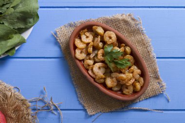 Lezzetli küçük kırmızı karides tereyağı ile baharat baharat haşlanmış. Geleneksel Yunan çanak çömlek içinde hizmet veren karides güveç. Üstten görünüm mavi rustik arka plan. En ortak gıda alerjenleri arasında diğer kabuklu deniz ürünleri.