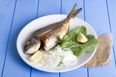 Yeşil ve mavi ahşap masa, deniz ürünleri kavramı üzerinde limon ile ızgara dorado balık