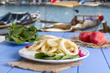 Lezzetli derin kızarmış kalamar garson beyaz daire plaka, kırmızı lahana, tartar, halka dilimlenmiş soğan ve yeşil roka salatası rustik mavi ahşap arka plan üzerinde. Kalamar çok mutfaklarının yemek. Üstten görünüm.