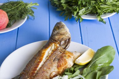 Yeşil ve mavi ahşap masa, deniz ürünleri kavramı üzerinde limon ile ızgara levrek balık