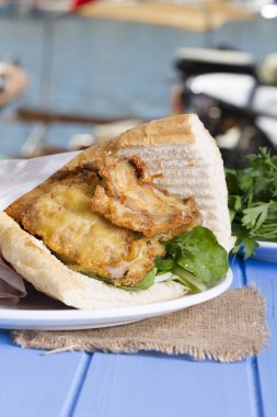 Mavi ahşap masada açık havada lezzetli kızarmış balık sandviç