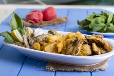 Lezzetli derin kızarmış Mix deniz ürünleri balık plaka mezgit, hamsi, sardalya, mavi rustik ahşap arka plan üzerinde beyaz soğan, limon, domates, roka salatası dilimlenmiş.