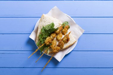 Lezzetli altın derin kızarmış pirzola midye şişleri yoğurt sos tartar ile hizmet veren sandviç, domates, dilimlenmiş beyaz soğan, maydanoz ve yeşil roka salatası mavi rustik masa arka plan üzerinde. Midye tava ekmek.