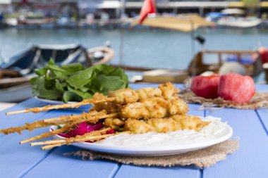 Lezzetli altın derin kızarmış pirzola midye yoğurt sos tartar ile hizmet veren şişleri, domates, dilimlenmiş beyaz soğan, maydanoz ve yeşil roka salatası mavi rustik masa arka plan üzerinde. Midye tava.