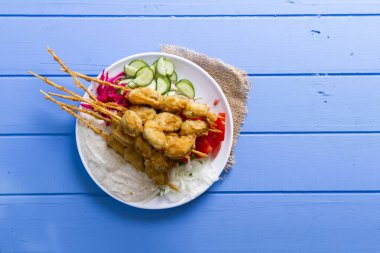 Lezzetli altın derin kızarmış pirzola midye yoğurt sos tartar ile hizmet veren şişleri, domates, dilimlenmiş beyaz soğan, maydanoz ve yeşil roka salatası mavi rustik masa arka plan üzerinde. Midye tava.