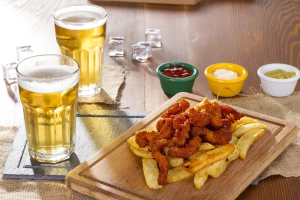 Köpüklü altın soğutulmuş bardak soğuk fıçı bira lezzetli sıcak gevrek ev yapımı taze kızarmış tabak içinde tavuk kanatları, dilimlenmiş domuz sosisi ve patates kızartması ile servis